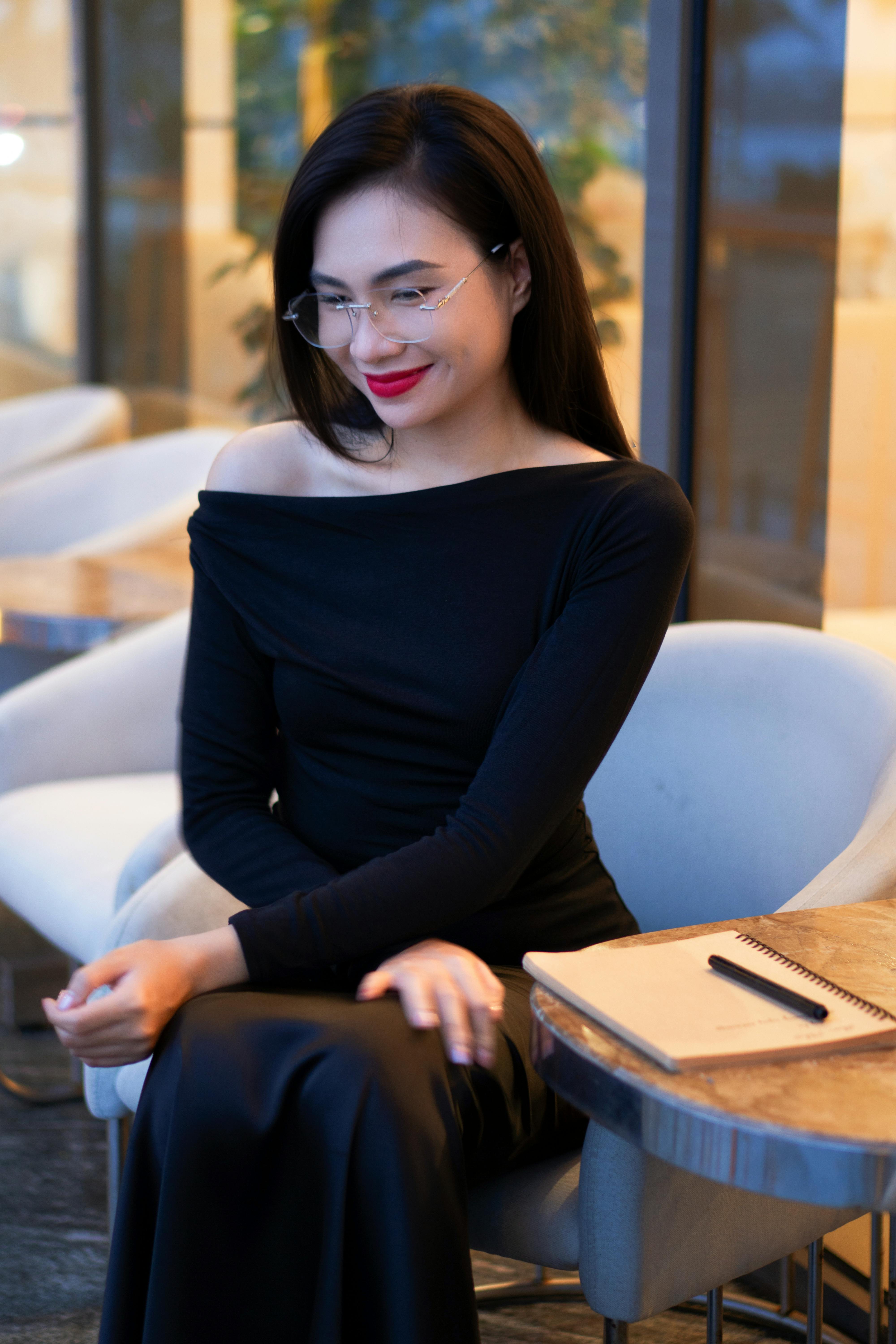 Sophisticated woman in a cafe setting, elegantly dressed in black with a notebook.