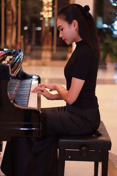A woman in formal attire plays a grand piano in an elegant indoor setting.