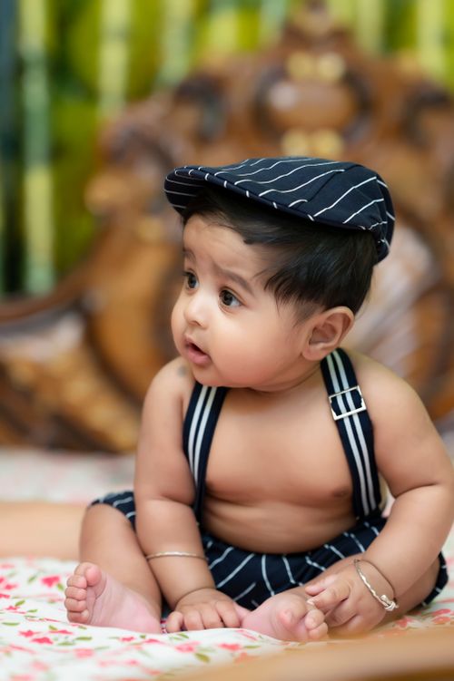 Free Cute baby sitting indoors wearing a striped cap and suspenders, with vibrant background. Stock Photo