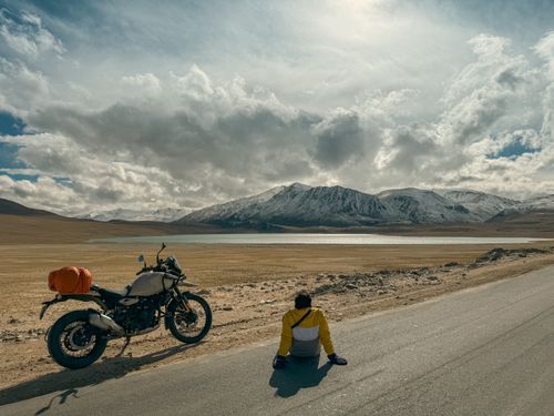 Free Traveler relaxing beside a motorcycle with stunning mountain and lake view in sunny weather. Stock Photo