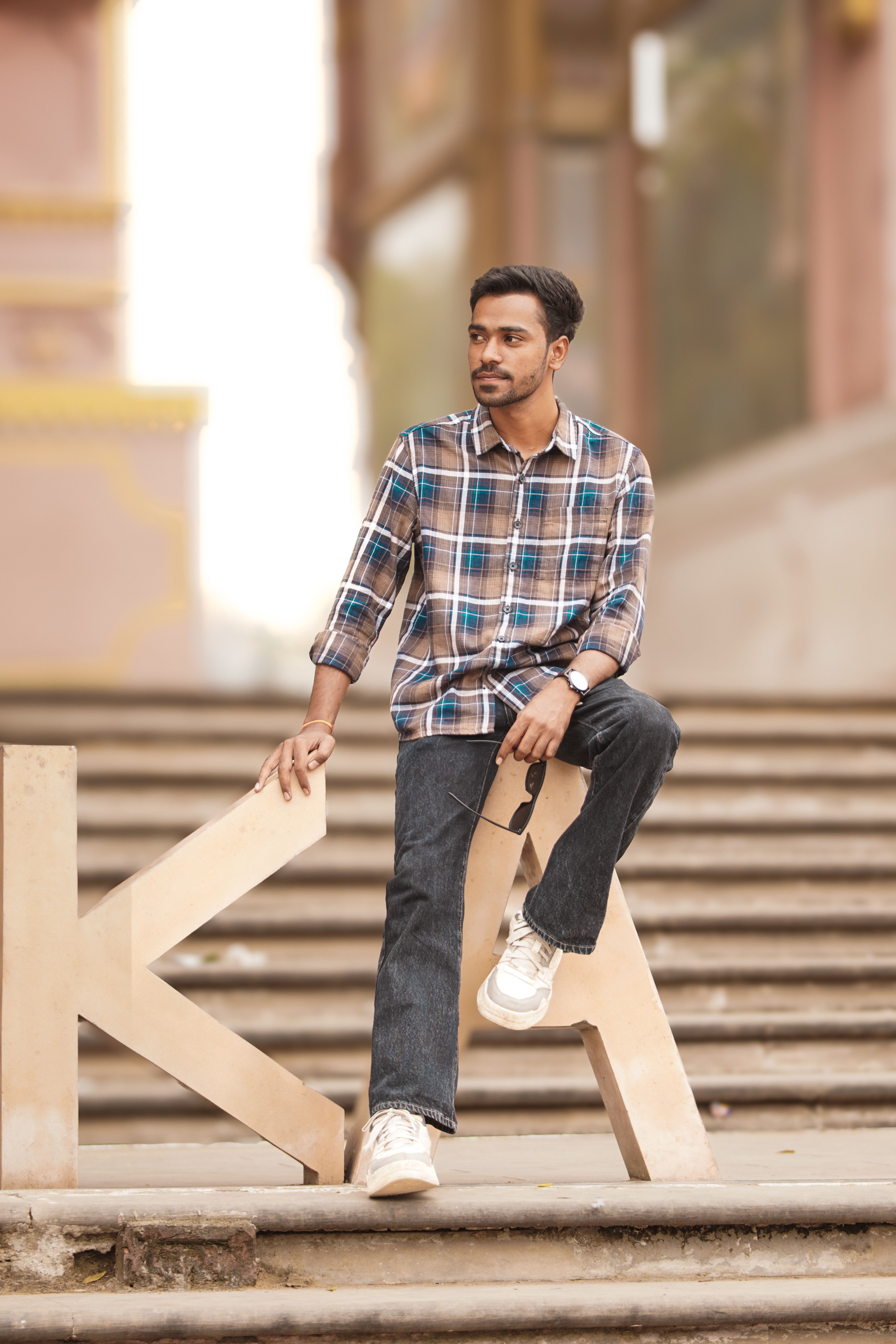 Young man in plaid shirt sitting on steps, relaxed urban style.