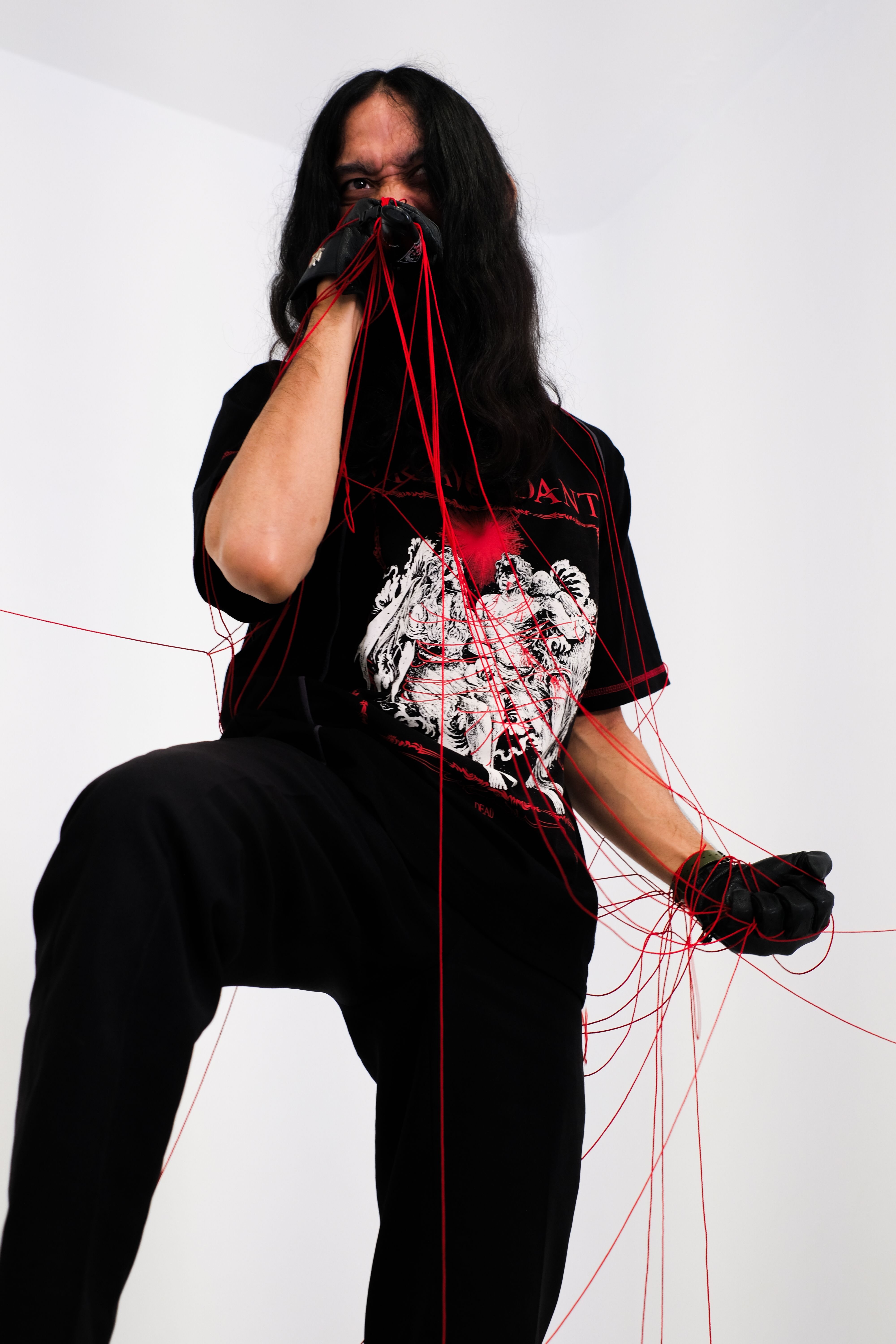 A striking portrait of a person entangled in red threads, wearing a black glove.
