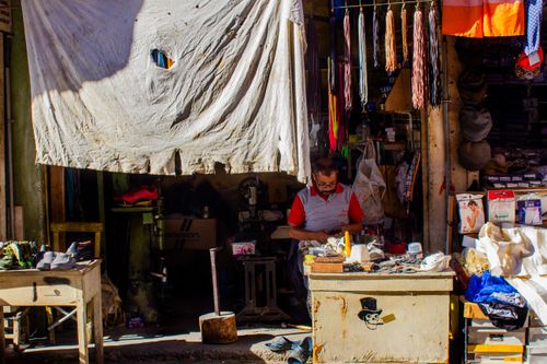 Free Cobbler working in a traditional shoe repair shop with fabrics and tools. Stock Photo