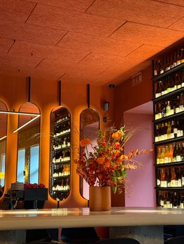 Sophisticated bar interior featuring vibrant orange floral display with wine bottles on shelves.