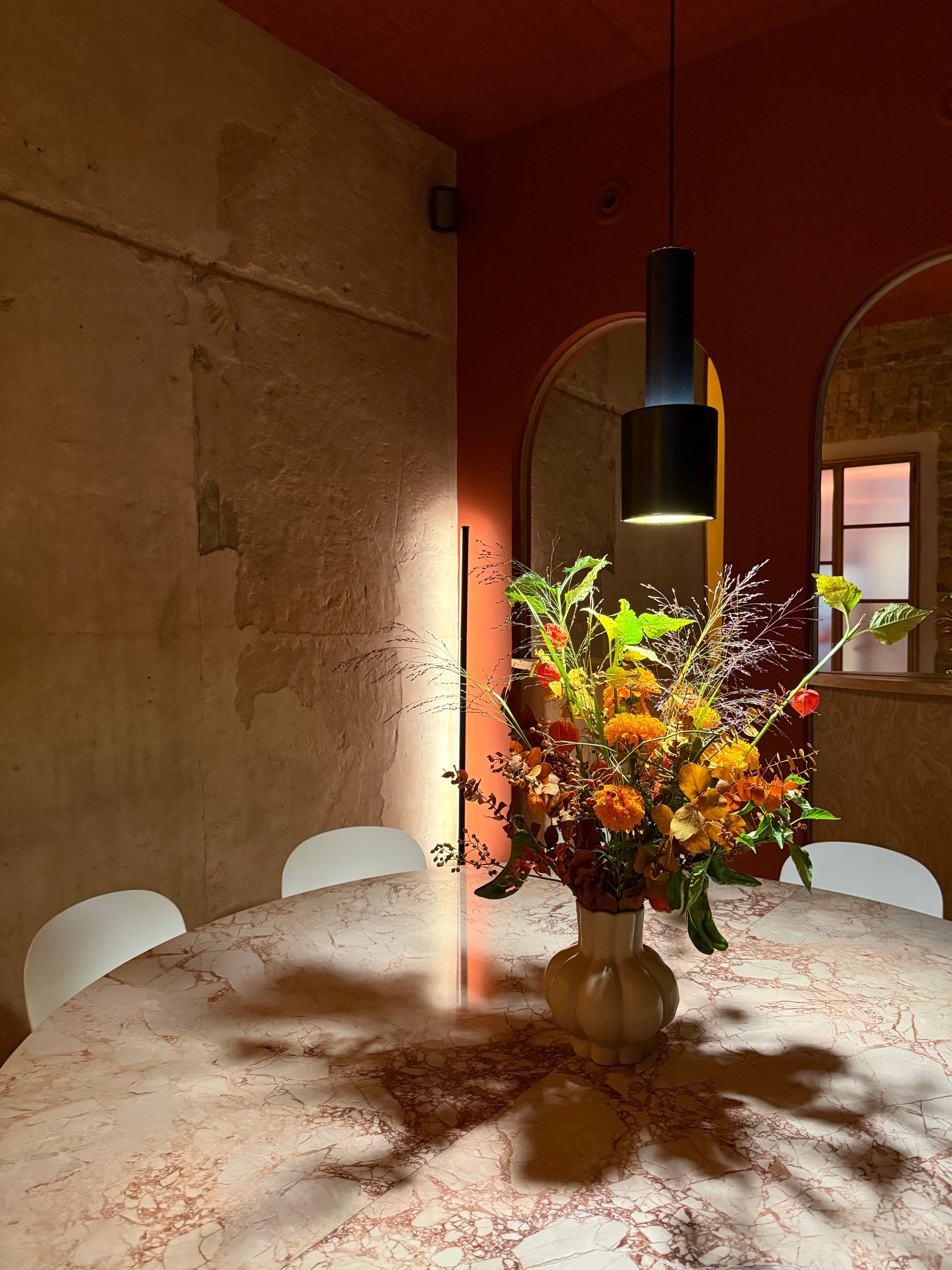 A beautifully lit dining room with a vibrant floral arrangement on a round marble table.