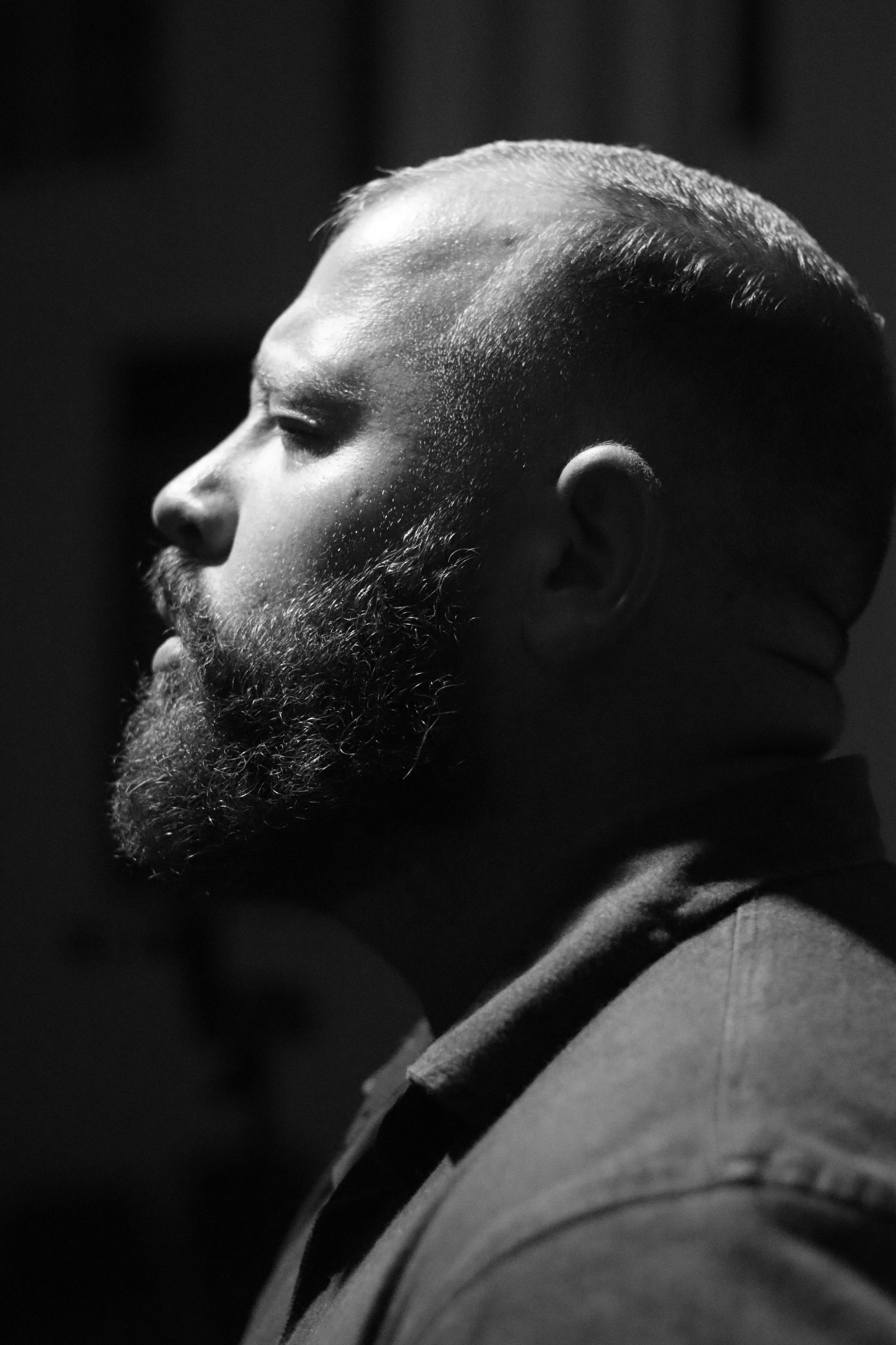Black and white side profile portrait of a bearded man with dramatic lighting.
