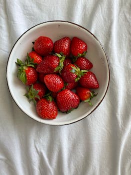 A vibrant bowl of fresh strawberries resting on a white surface, perfect for summer.