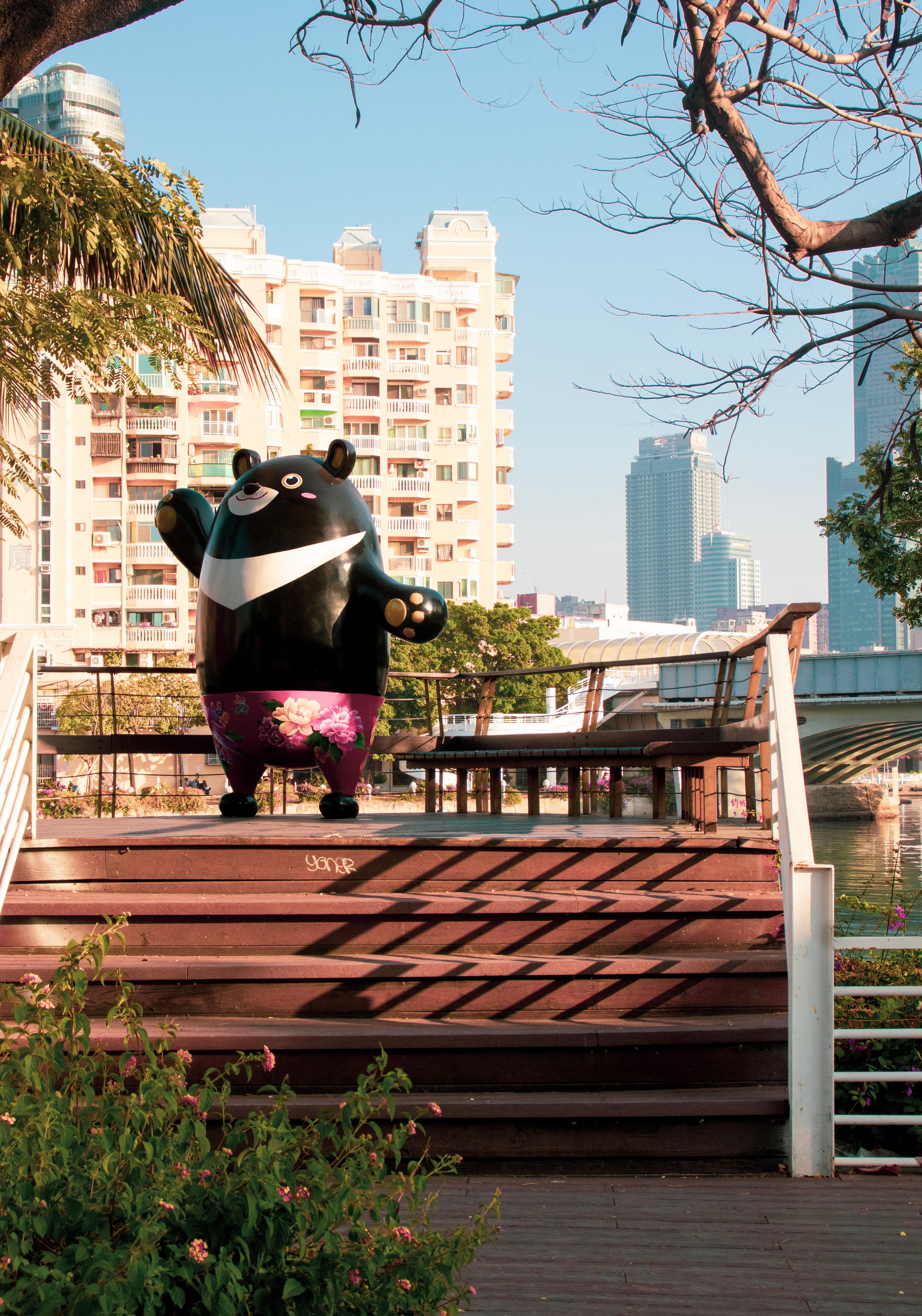 Vibrant bear statue on wooden steps in a city park with high-rise buildings in background.