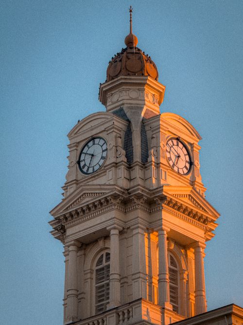 Free A classic clock tower lit by golden sunset light against a clear sky. Stock Photo