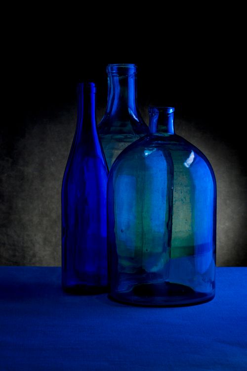 Free Dramatic still life of three vintage blue glass bottles against a dark backdrop, creating a moody aesthetic. Stock Photo