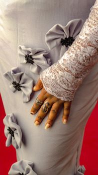 Close-up of a lace dress adorned with flowers, showcasing hand jewelry and intricate textures.