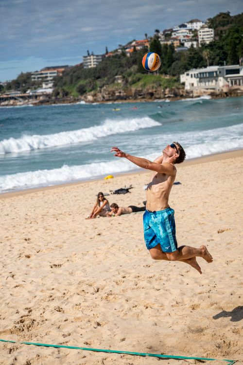 Free Action-packed beach volleyball scene with man jumping to hit the ball against a scenic seaside backdrop. Stock Photo