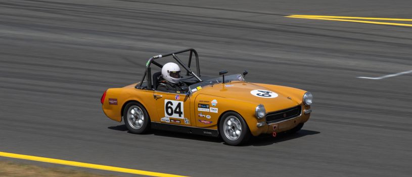 A classic orange racing car with number 64 speeding on a racing track driven by a helmeted driver.