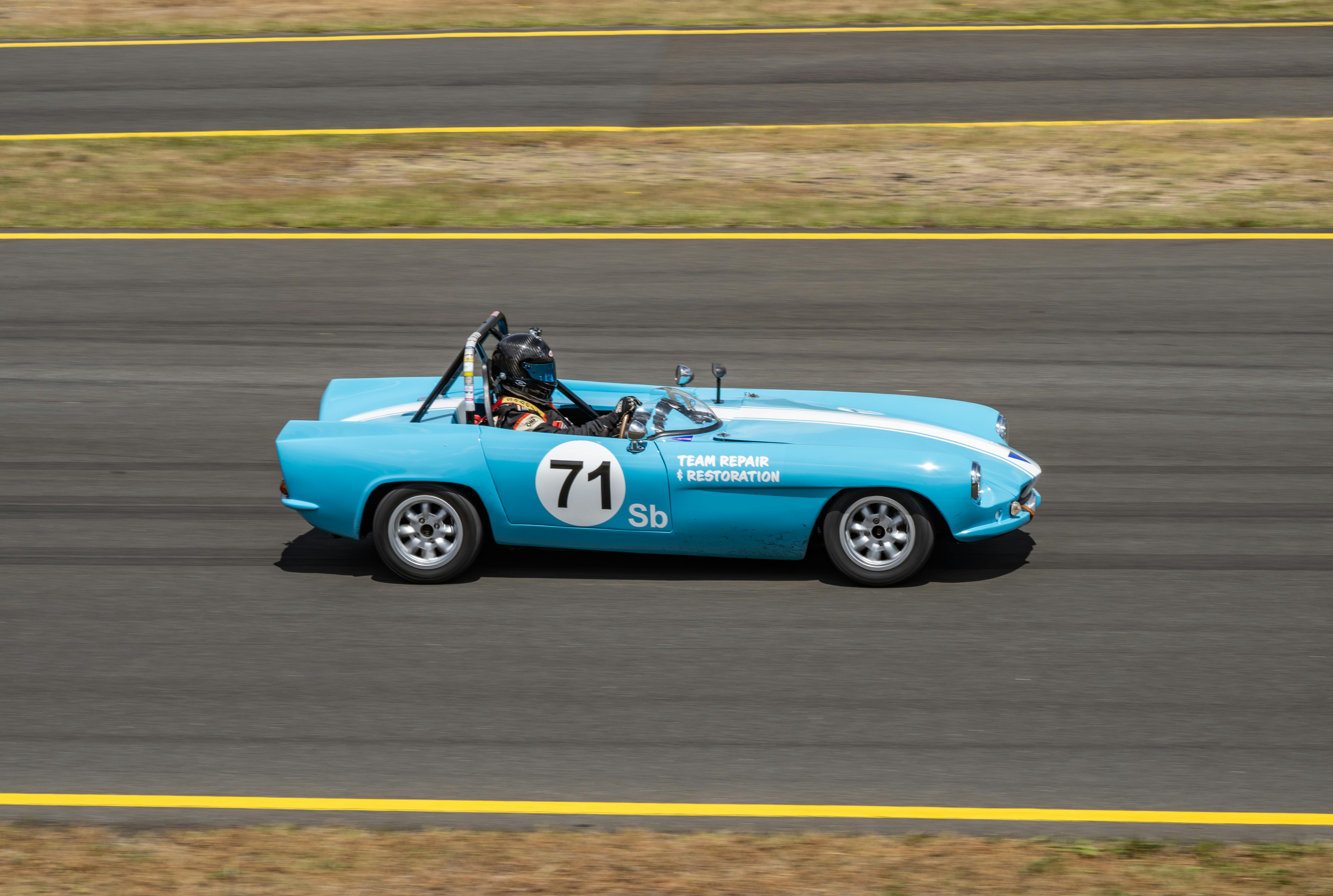 Blue vintage race car with number 71 speeding along a track during a sunny day race.
