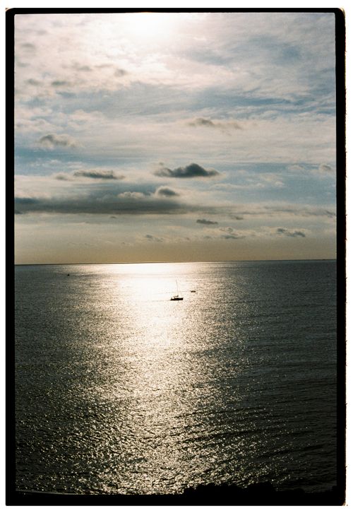 Free A tranquil ocean scene with a sailboat under a dramatic sunset sky. Stock Photo