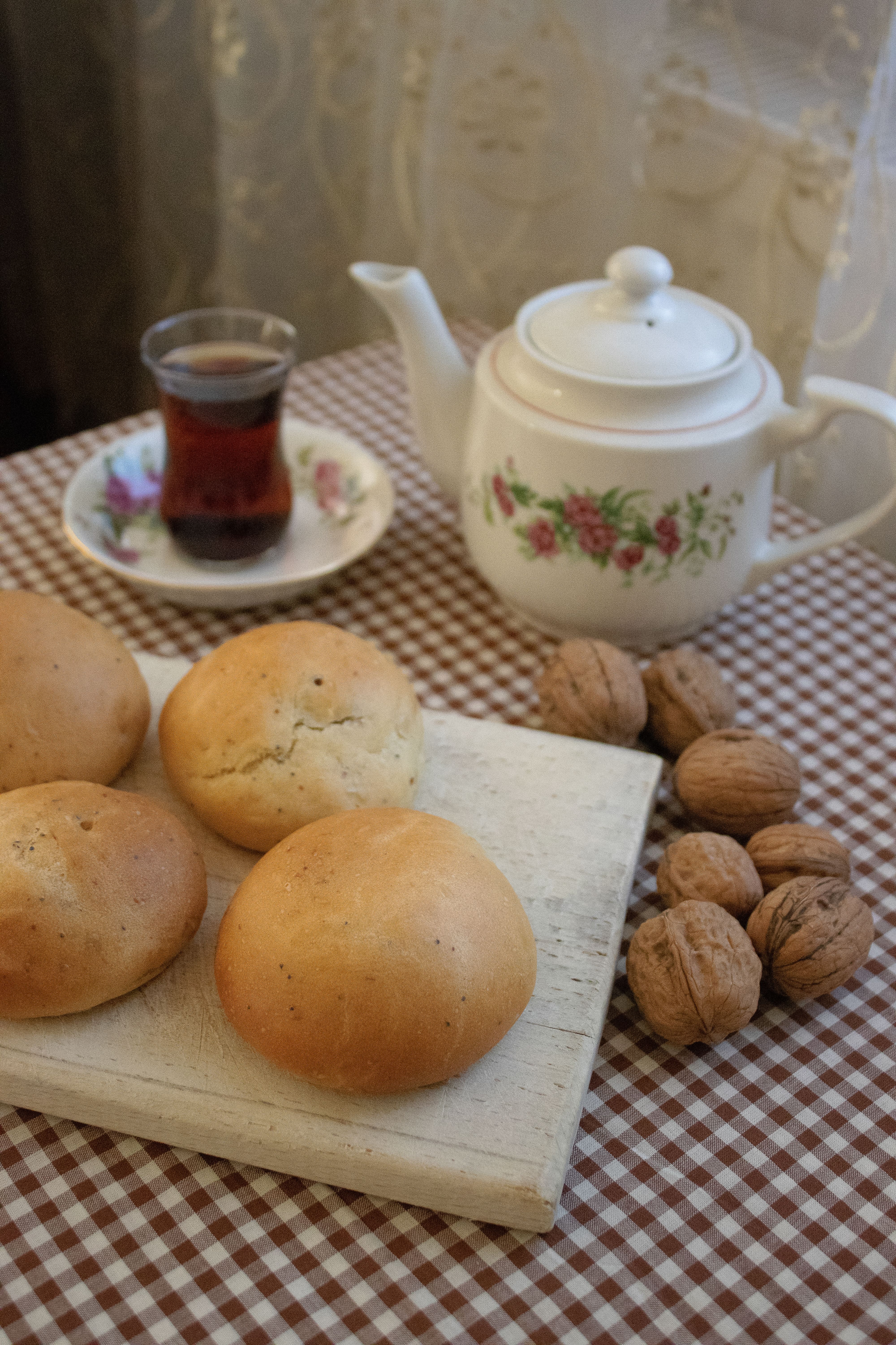 A warm and inviting tea setup with buns, walnuts, and a floral teapot.