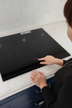 A person interacts with a sleek black induction cooktop in a modern kitchen setting.