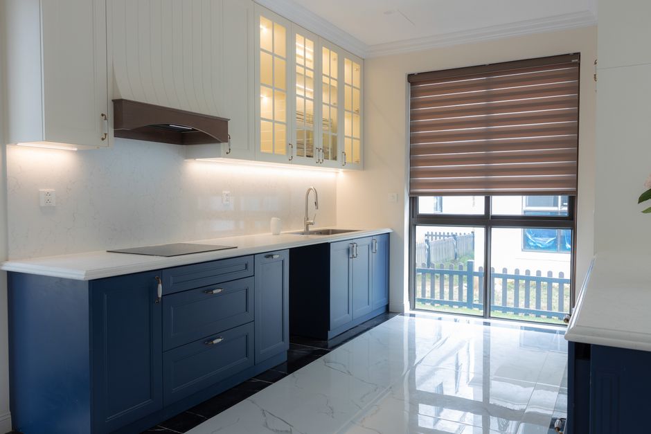 Bright modern kitchen featuring blue cabinetry, marble countertops, and ample natural light through large windows.