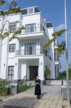 Contemporary white house exterior with a woman standing in front, clear blue sky.