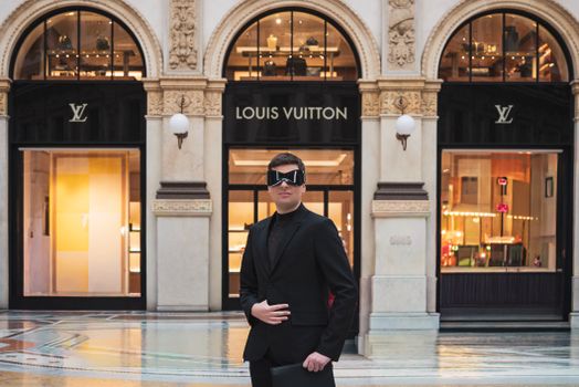 Stylish man in black suit and futuristic glasses poses at Galleria Vittorio Emanuele II.