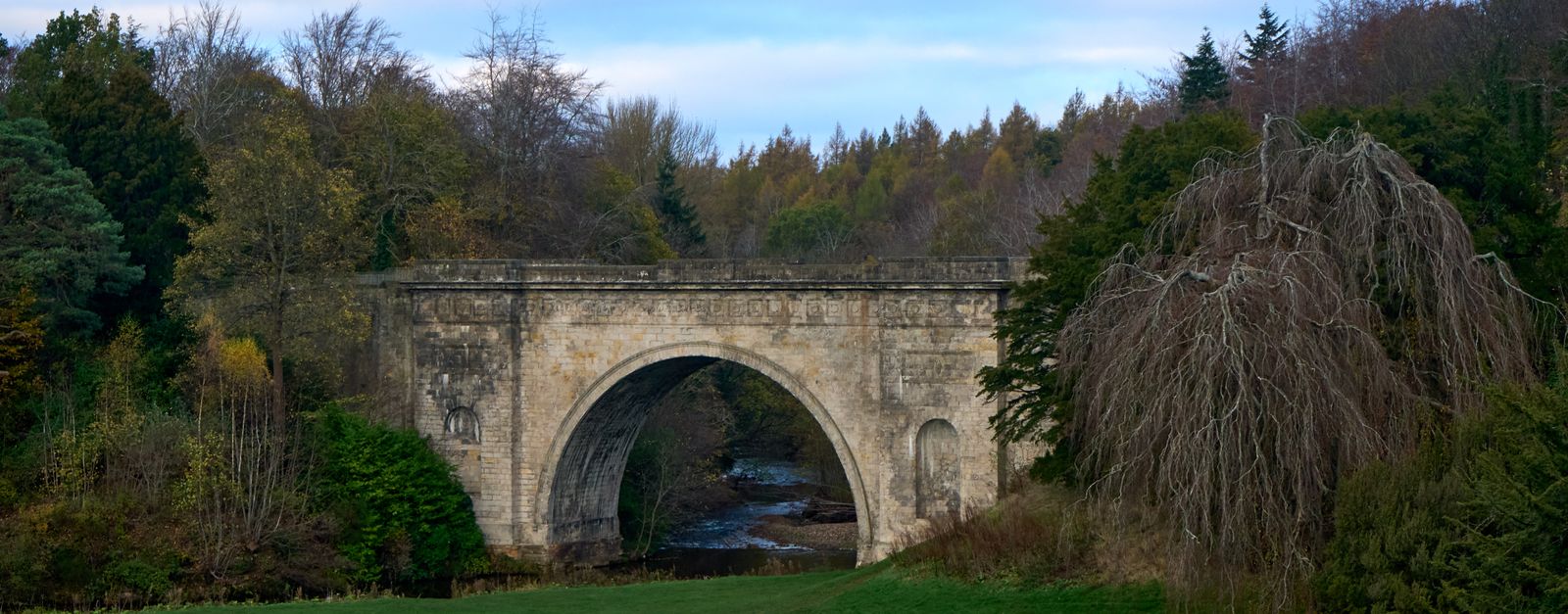 Stone arch bridge surrounded by fall foliage in a serene countryside setting.