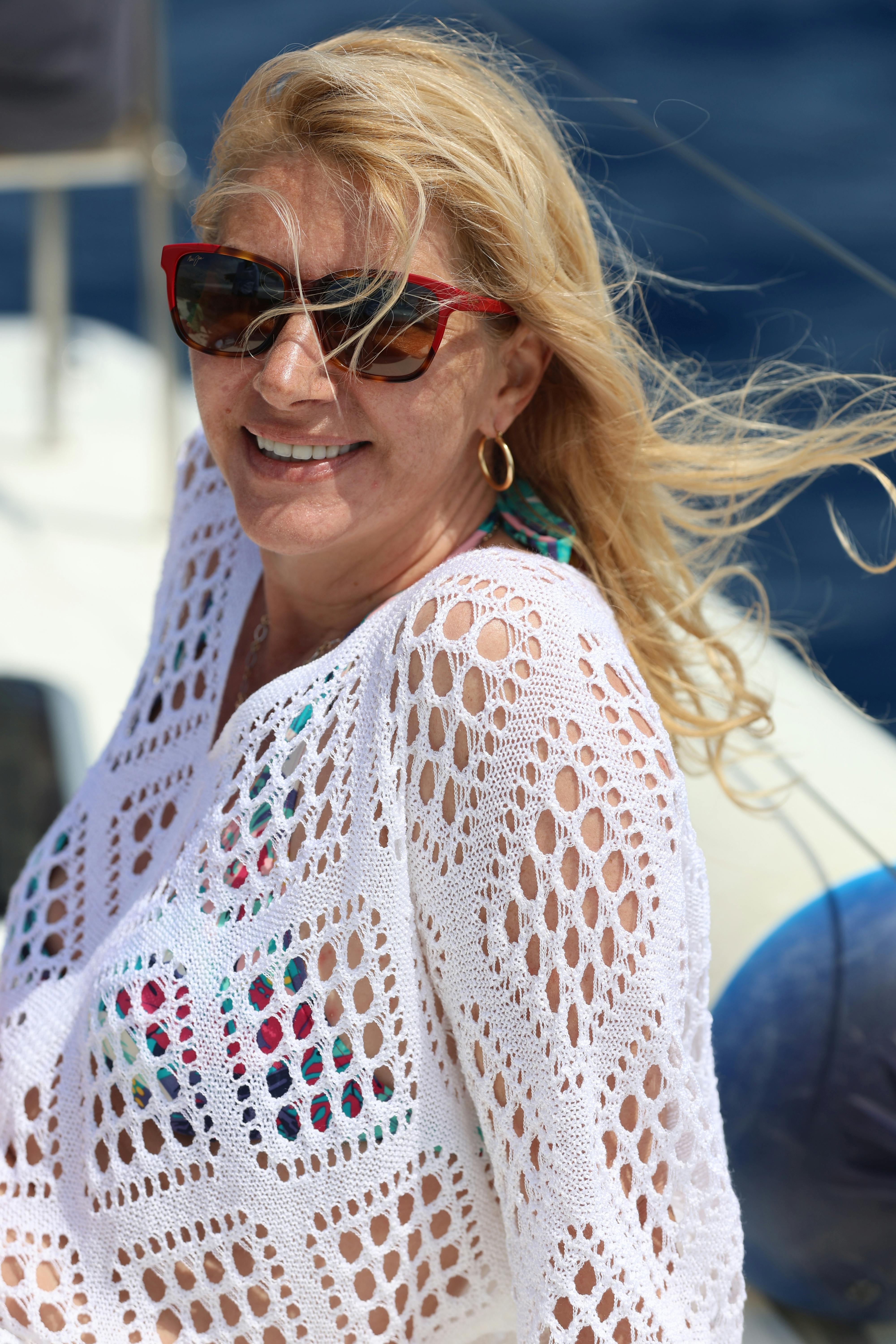 Cheerful woman with blonde hair and sunglasses enjoying a sunny day on a yacht.
