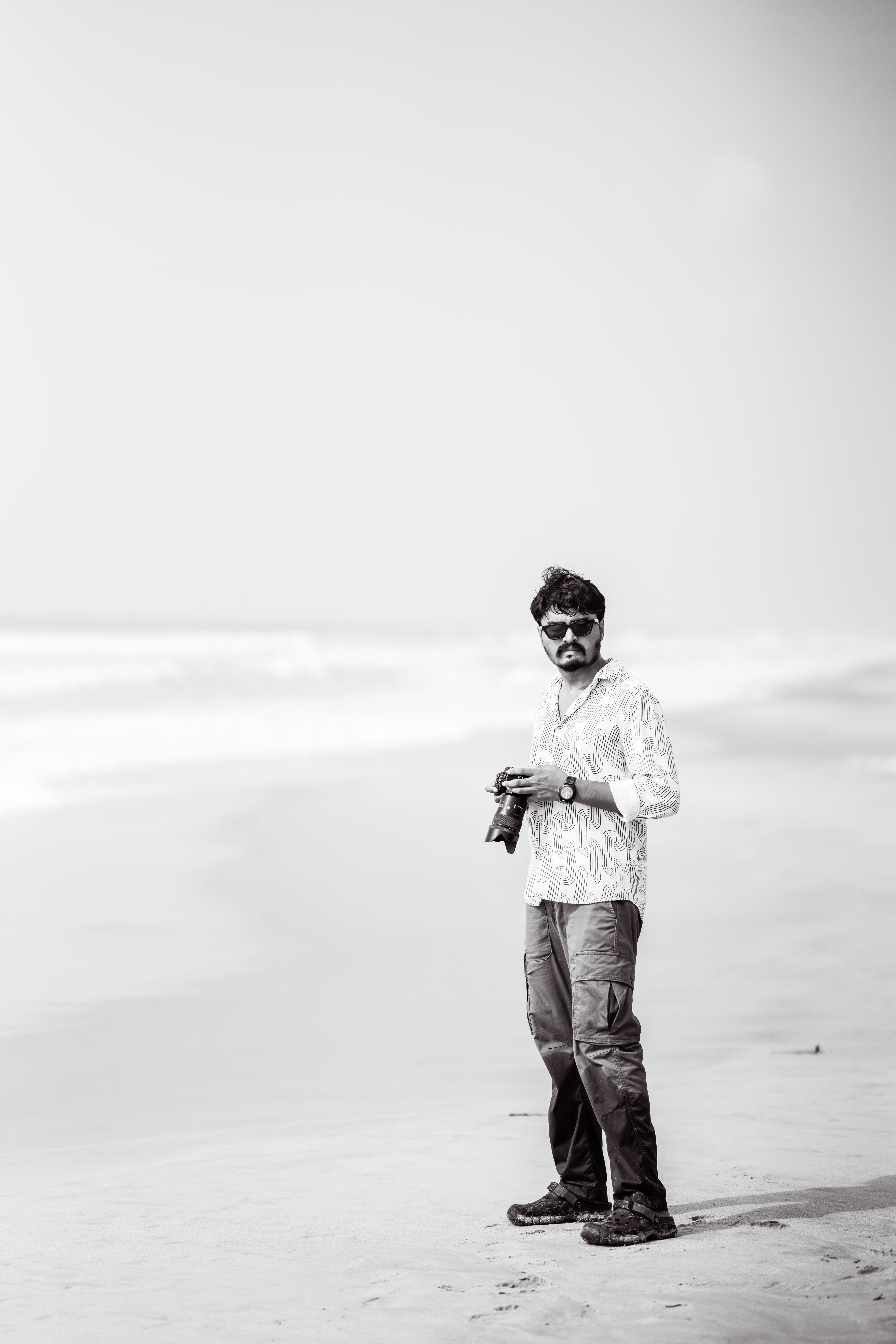 Captivating black and white photo of a man holding a camera on a serene beach