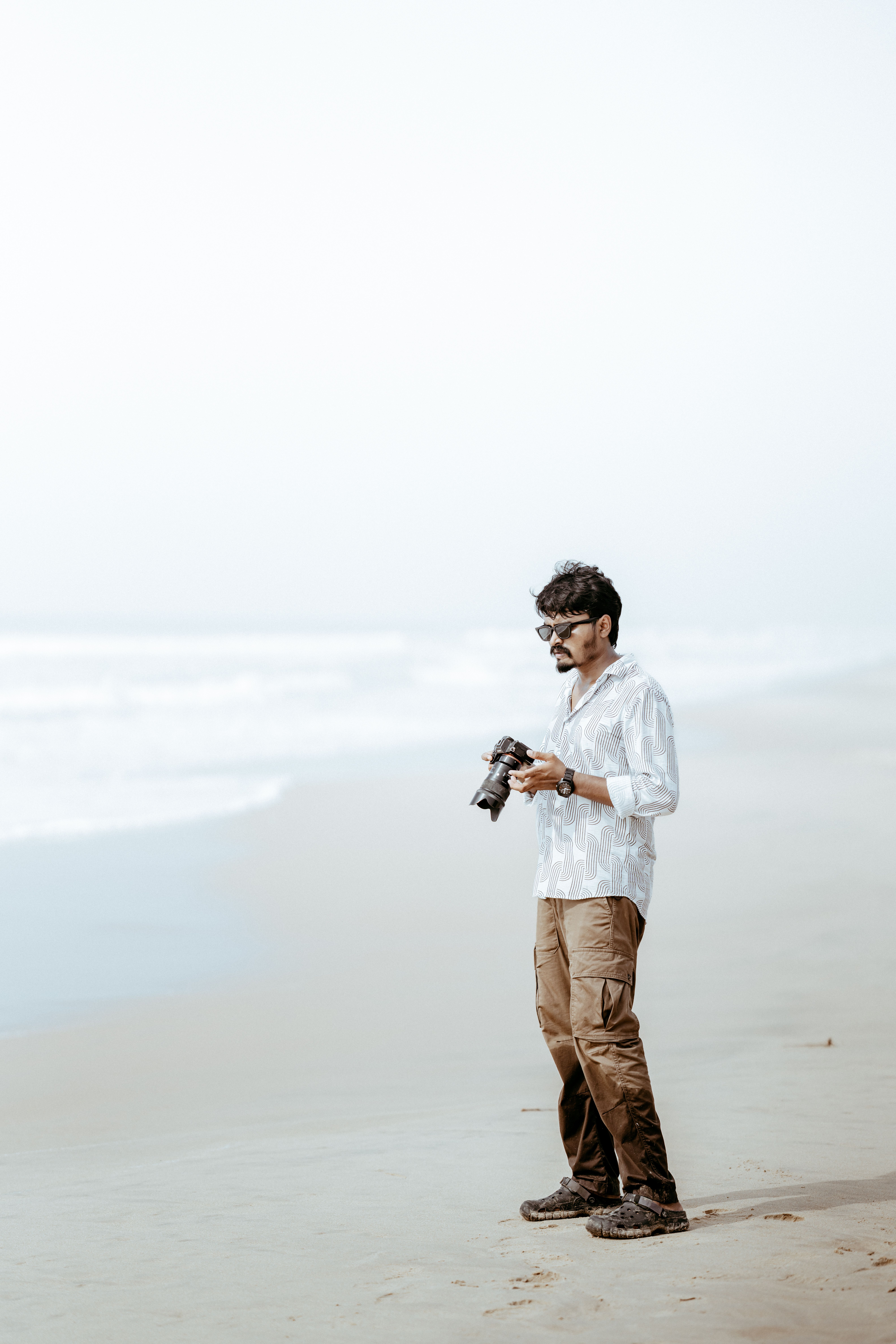 Man holding a camera on a tranquil beach, capturing serene ocean views.