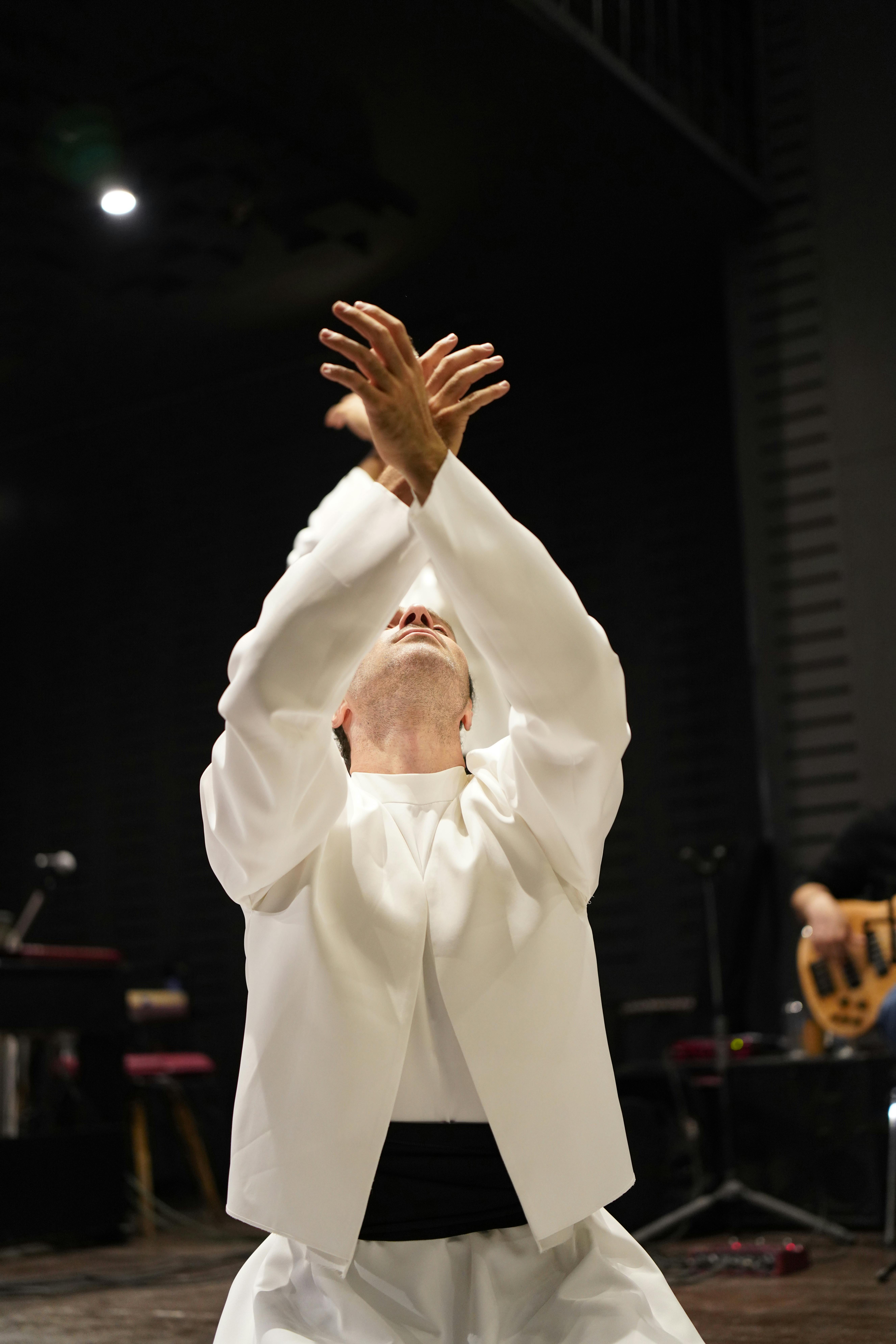 Free A dance performer in a white robe performs expressively on stage, reaching upward. Stock Photo