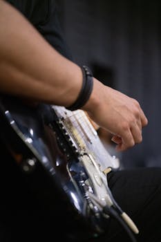 Detailed shot of a musician's hand playing an electric guitar in a studio setting, emphasizing musical artistry.