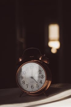A copper vintage alarm clock glowing in soft morning light, casting shadows.