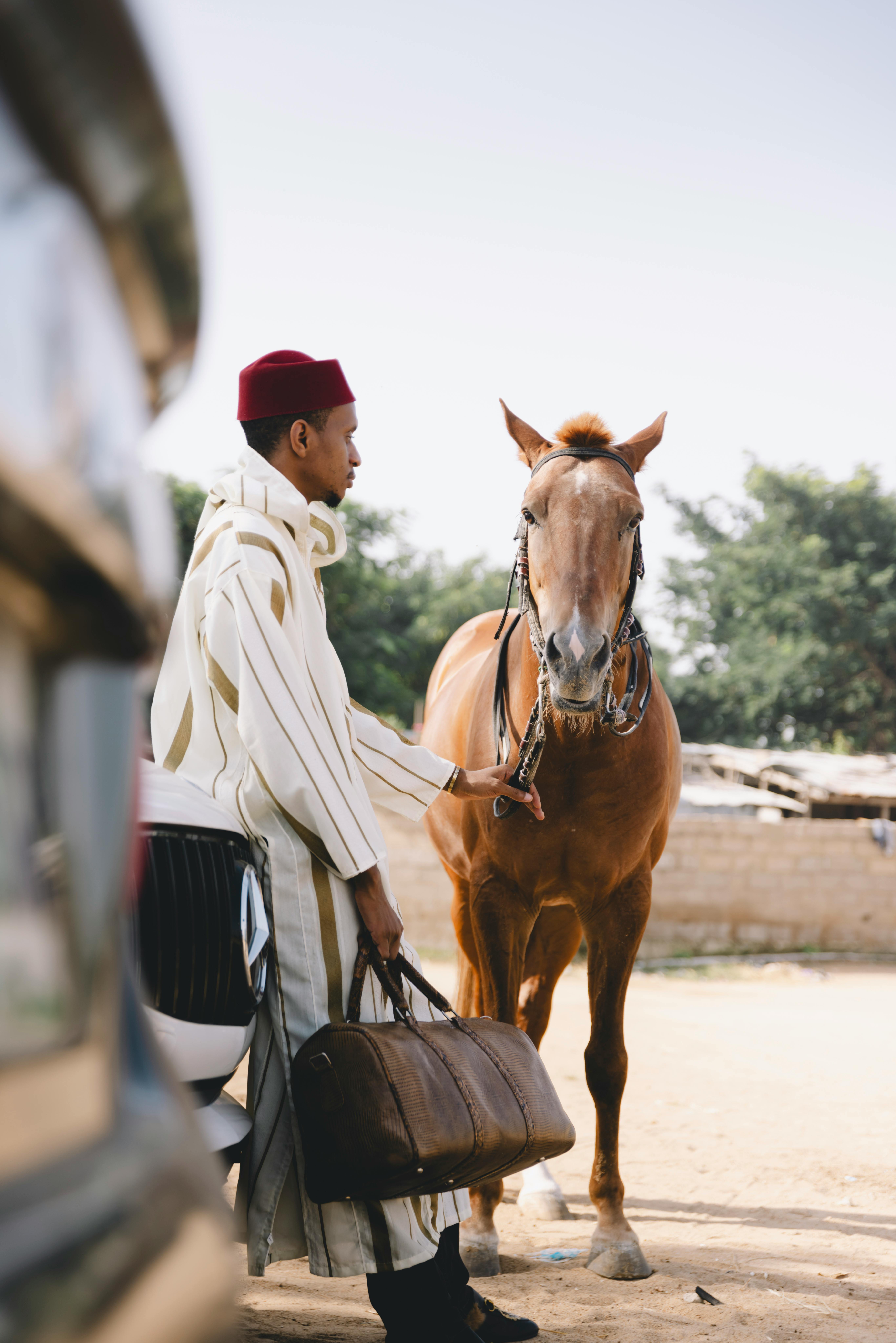 Man in traditional clothing stands beside a horse, outdoors, showcasing cultural heritage.
