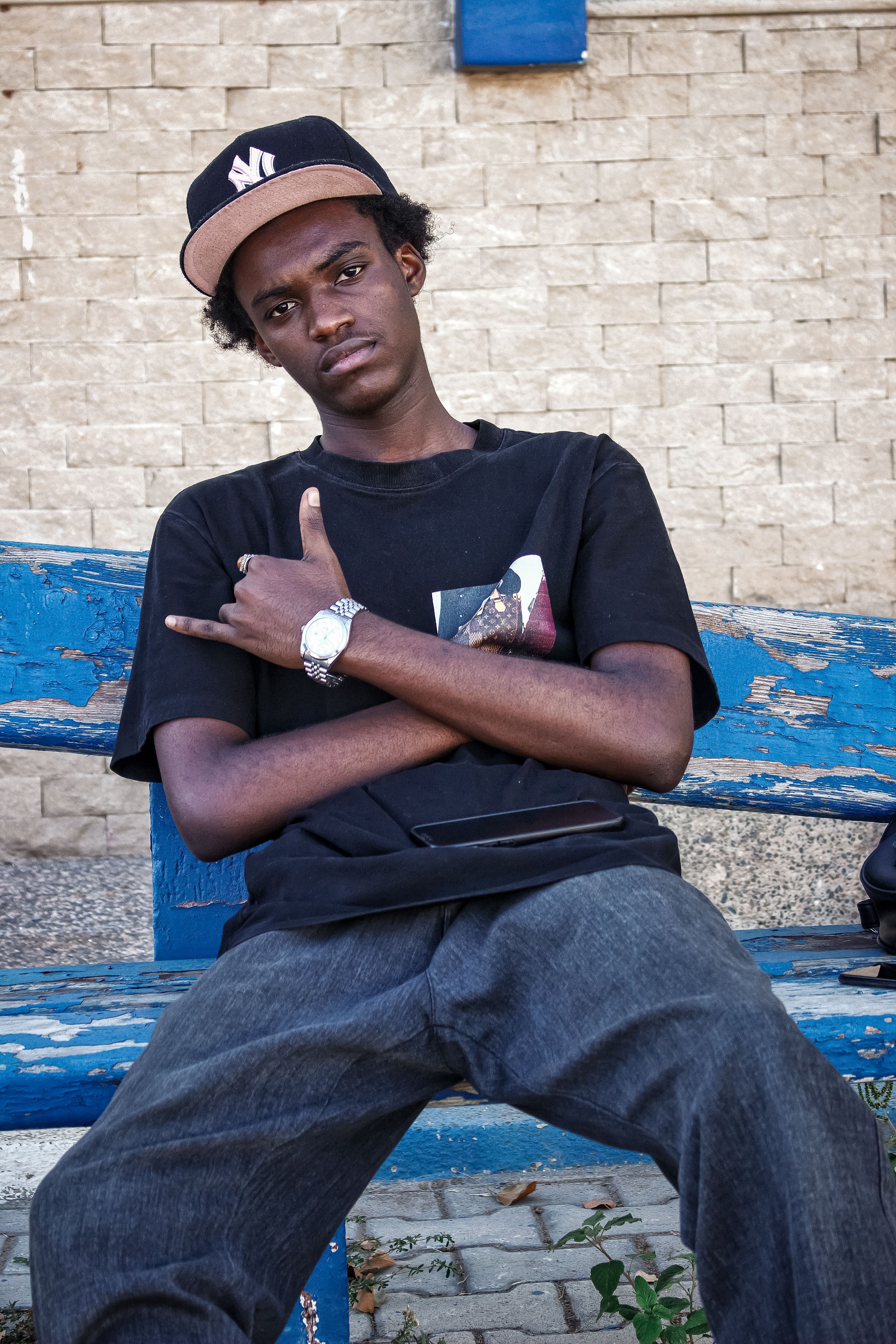 Young man in casual attire sits on a blue bench outdoors, exuding a relaxed urban vibe.