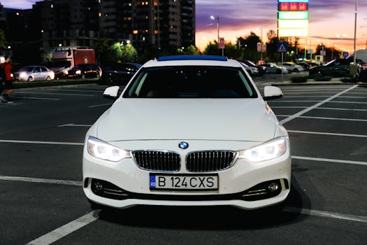 White BMW car in a parking lot at sunset, urban setting with city lights and buildings in the background.
