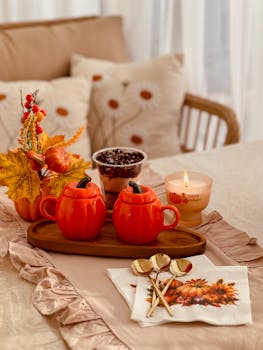 Warm autumn setting with pumpkin mugs, candle, and fall leaves on a cozy table.