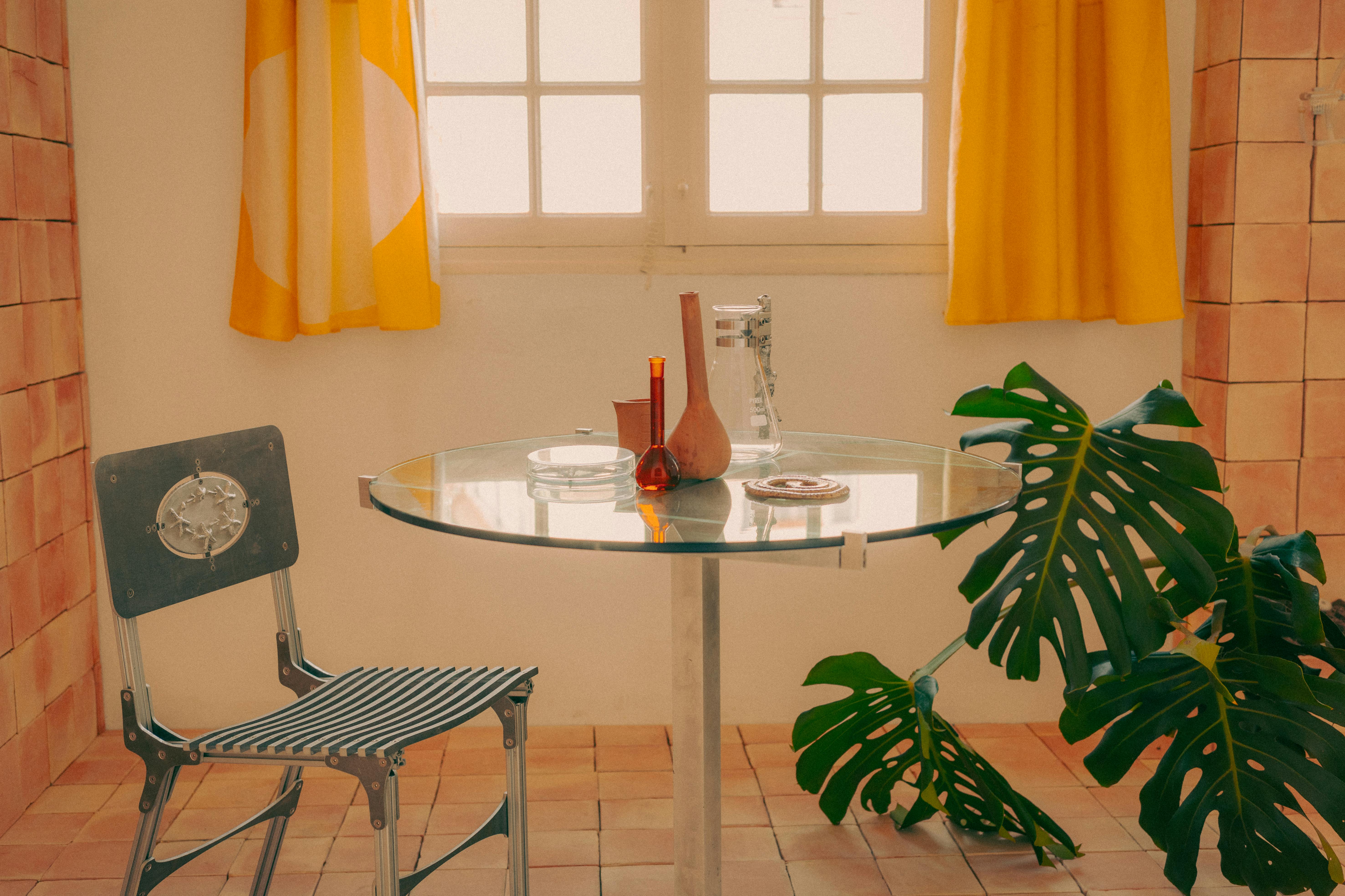 A cozy vintage-style room featuring a glass table, chair, and Monstera plant.
