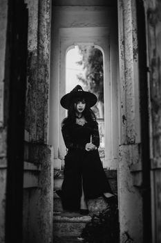 Black and white portrait of a woman in gothic attire sitting in an architectural setting.