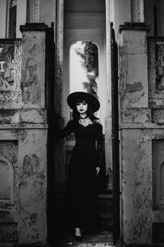 A woman in gothic attire stands in a vintage doorway, exuding an air of mystery.