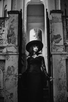 Black and white portrait of a woman in gothic attire standing in an old, rustic building.