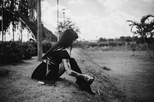 Contemplative woman sitting in a serene outdoor environment, captured in black and white.