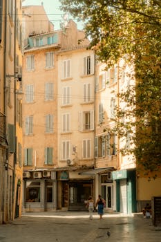 Golden light bathes a quaint European alleyway with pedestrians and shuttered windows.