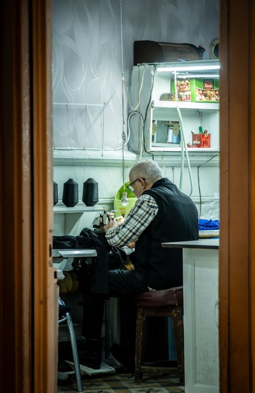 Free Elderly tailor focusing on sewing in a small, cozy workshop with subdued lighting. Stock Photo