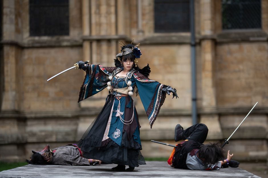 Cosplayers enact a dramatic scene with swords outside an ancient structure.