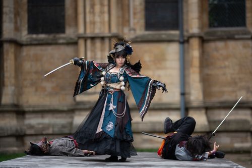 Free Cosplayers enact a dramatic scene with swords outside an ancient structure. Stock Photo