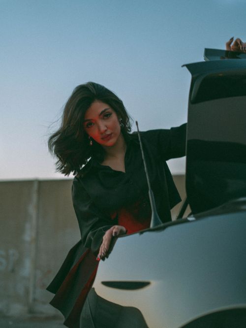 Free Elegant woman with short dark hair poses by an open car trunk at sunset, exuding confidence. Stock Photo