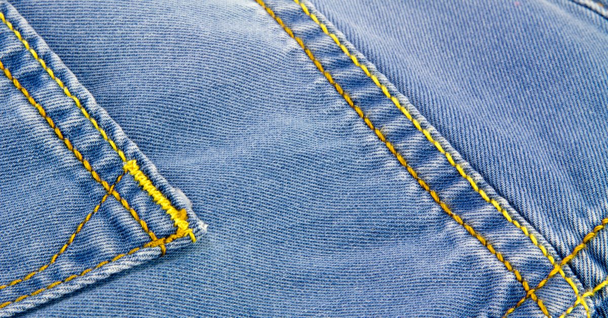 Detalhe em close-up de tecido jeans azul, mostrando costuras e textura em amarelo.