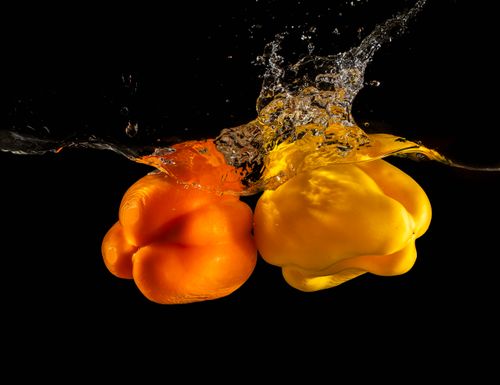 Free Orange and yellow bell peppers making a splash in water, against a black background. Stock Photo