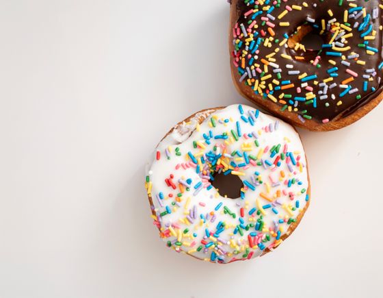 Two donuts, one with white icing and one with chocolate icing, covered in rainbow sprinkles