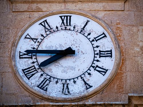 Free A classic stone clock tower face with aged, weathered Roman numerals and clock hands. Stock Photo