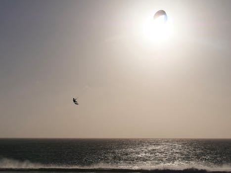A kitesurfer catching air over the sea beneath a bright sun in Tarifa, Spain.